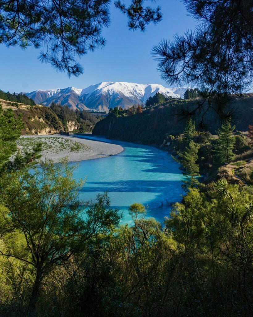 Rakia gorge, a beautiful scene with blue river, blue sky, and snow capped mountains. The images is framed with green tree leaves.